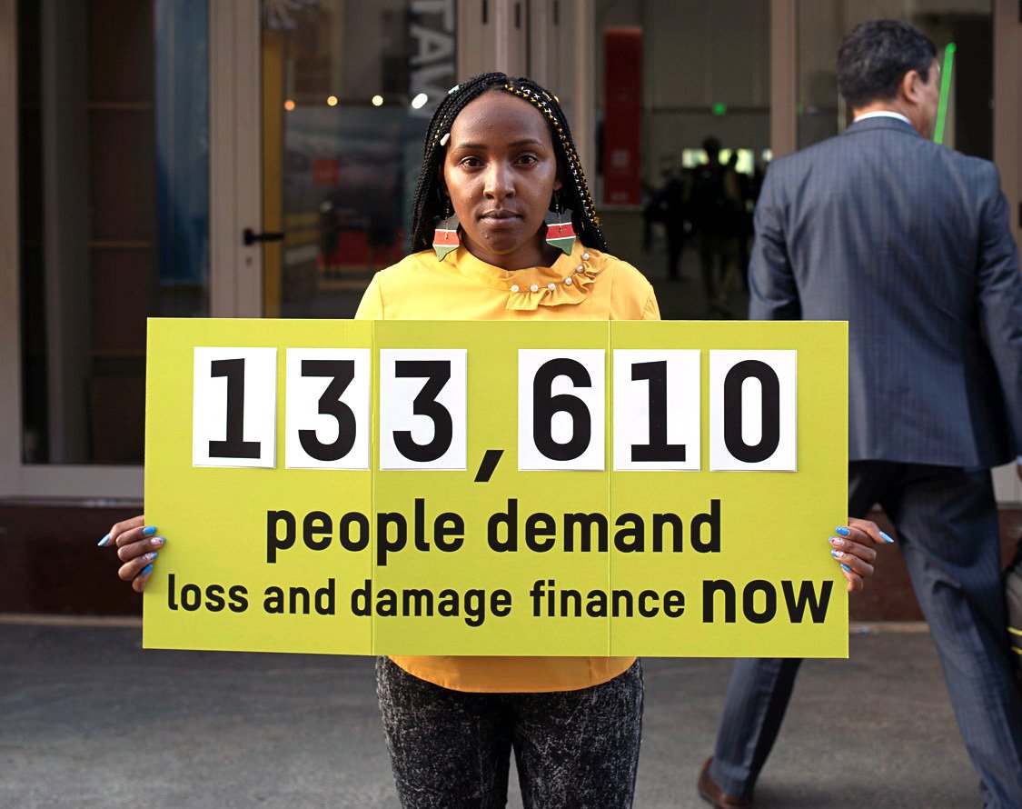 Elizabeth Wathuti holding sign: 133,610 people demand loss and damage finance now.
